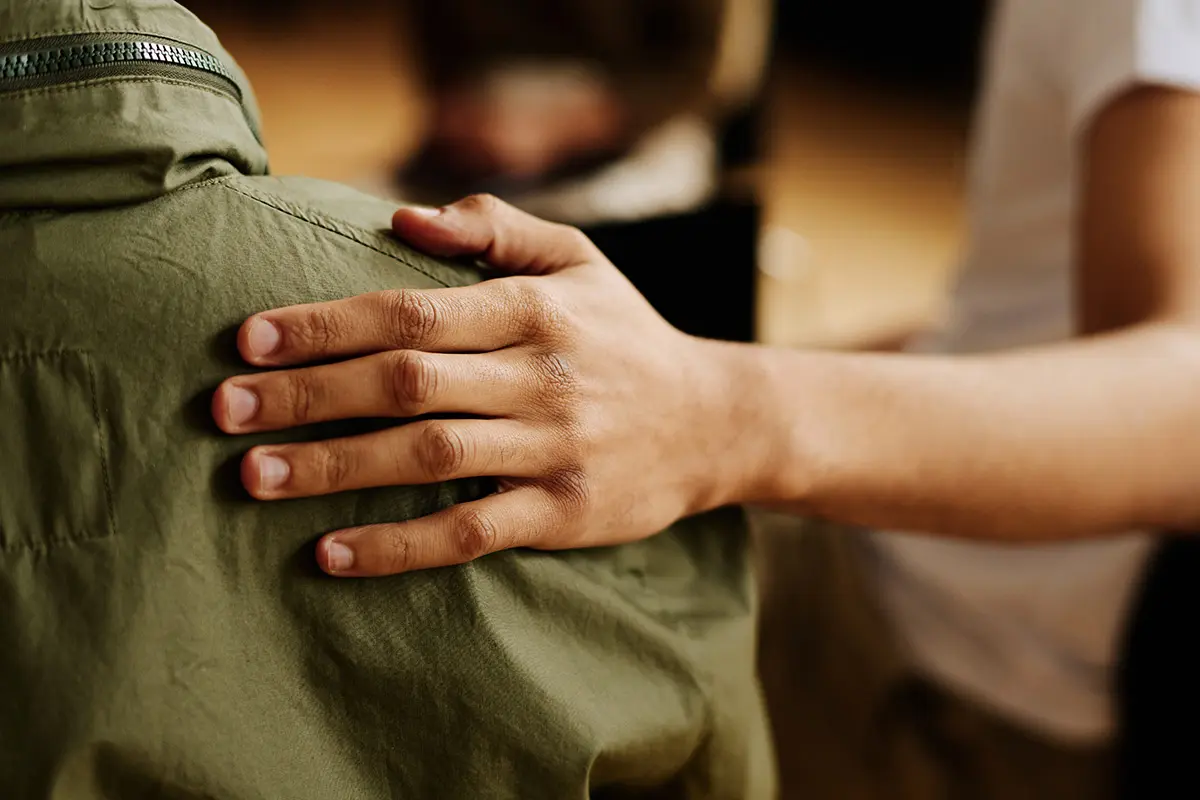 A person puts their hand on a friend's shoulder in support of their addiction recovery journey